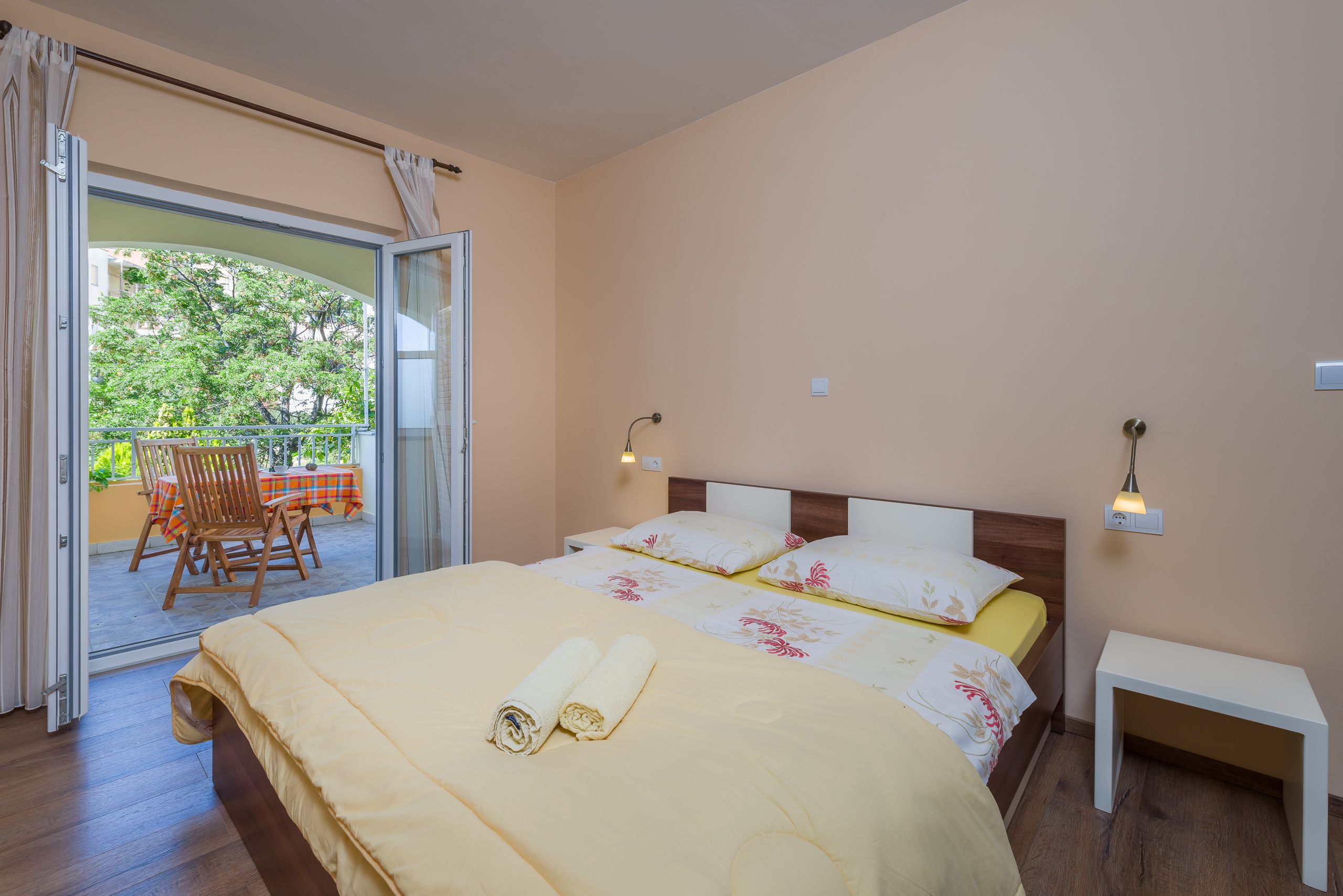 A bedroom with a bed, a nightstand, and a view of an outdoor area with a table and chairs.