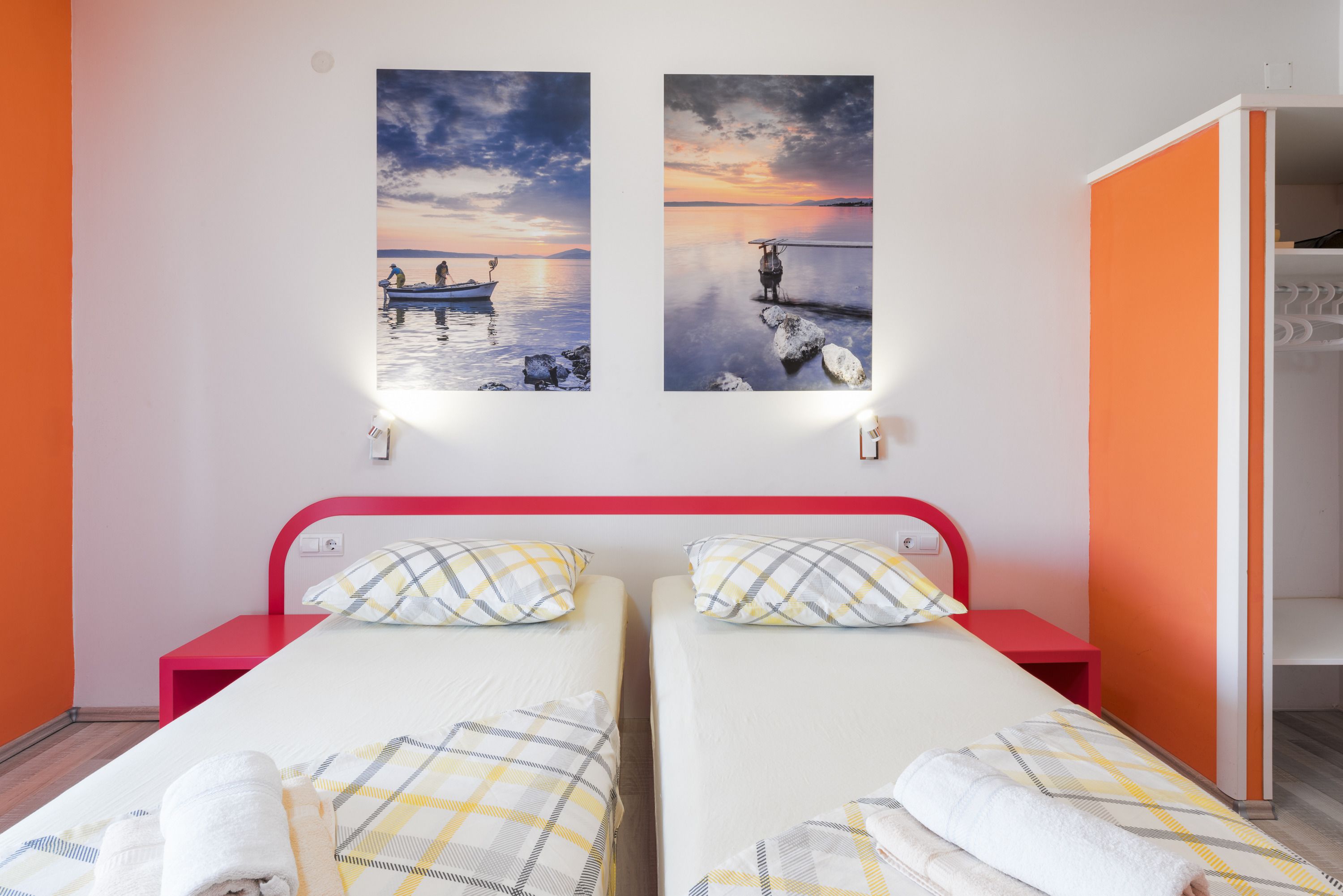 Ein Zimmer mit zwei Betten, jeweils mit Kopfkissen und Decke, sowie einem roten Kopfteil.