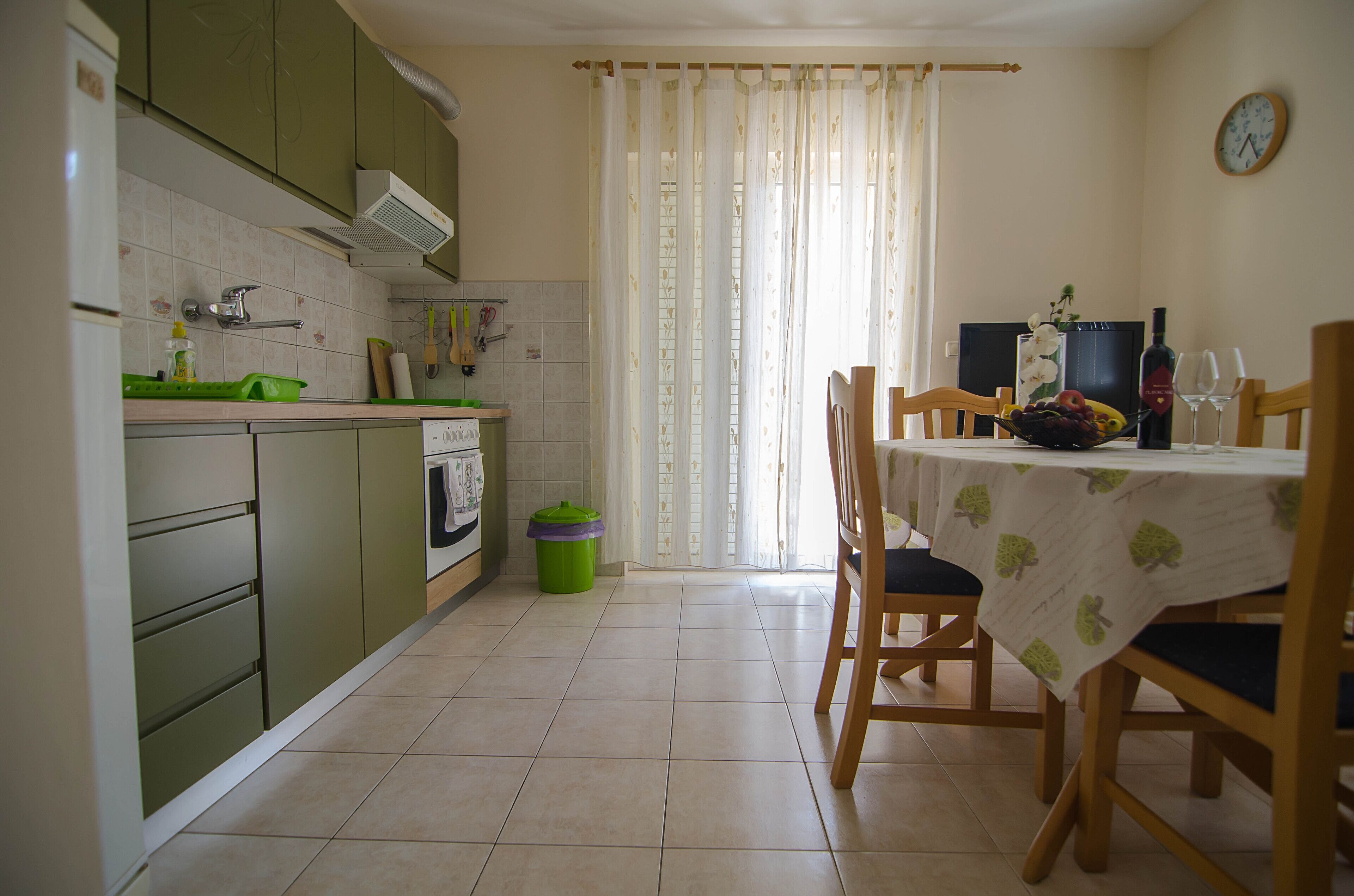 A kitchen with green cabinets, a dining table with a tablecloth, and a window with curtains.