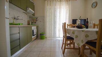A kitchen with green cabinets, a dining table with a tablecloth, and a window with curtains.