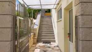 A covered outdoor staircase leading to a building entrance, with a metal gate on the left and a door on the right.