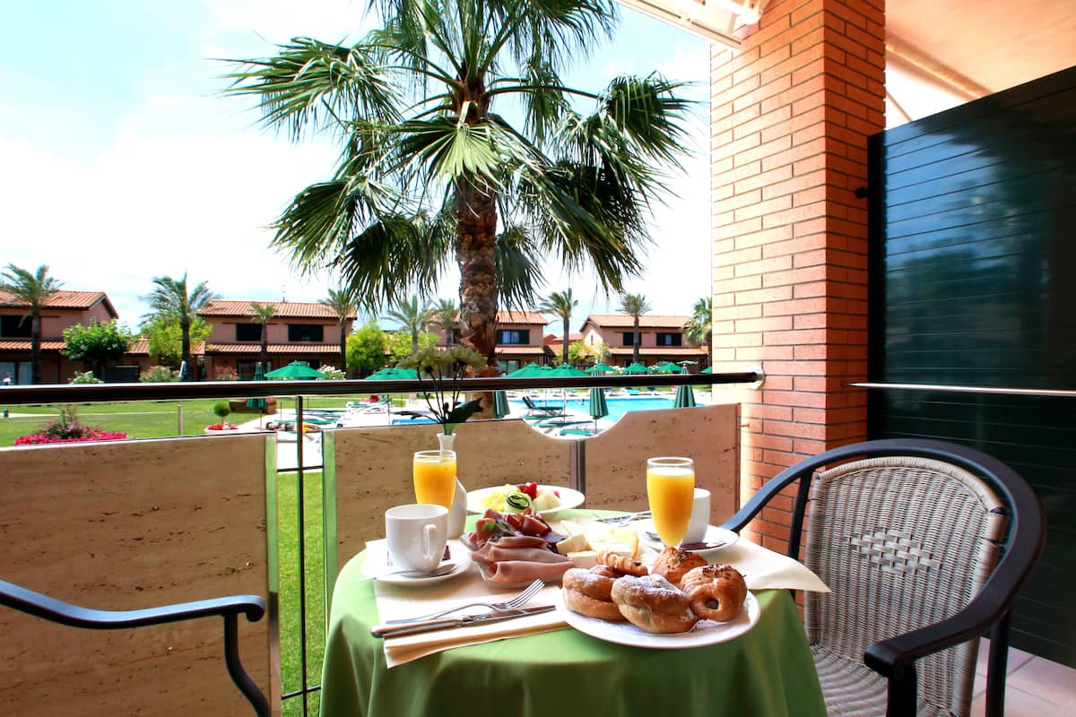 Une table sur le balcon avec des éléments pour le petit-déjeuner, un palmier et une vue sur la piscine.