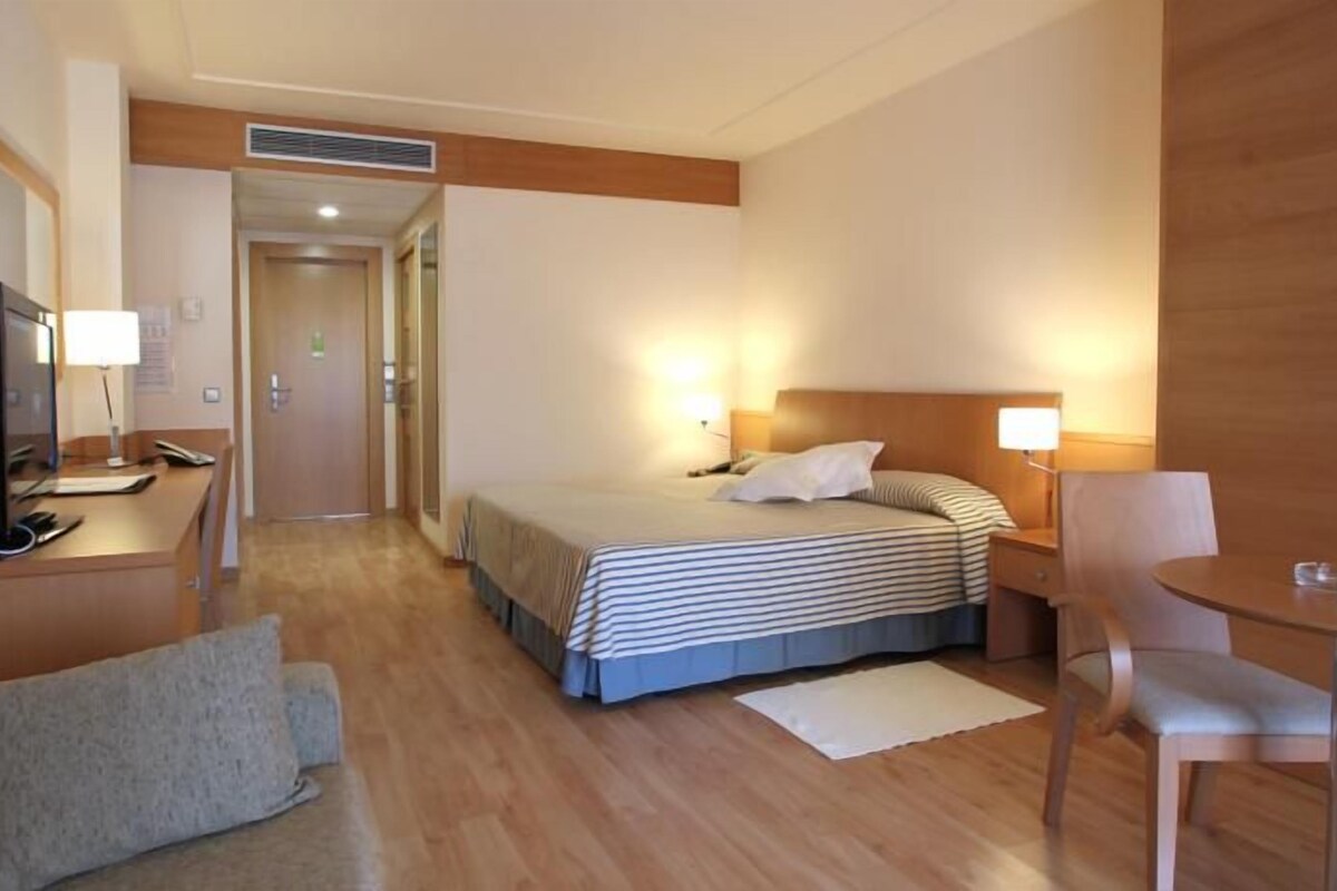 Een hotelkamer met een bed, een bureau met een computer, een stoel en een bijzettafeltje.