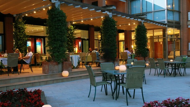 Un espace de restauration en plein air, avec des tables et des chaises, entouré de plantes en pot et illuminé de guirlandes lumineuses décoratives.