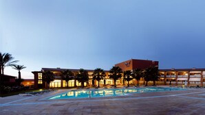 Un hôtel doté d’une piscine, de palmiers et d’un grand bâtiment agrémenté de nombreux balcons.