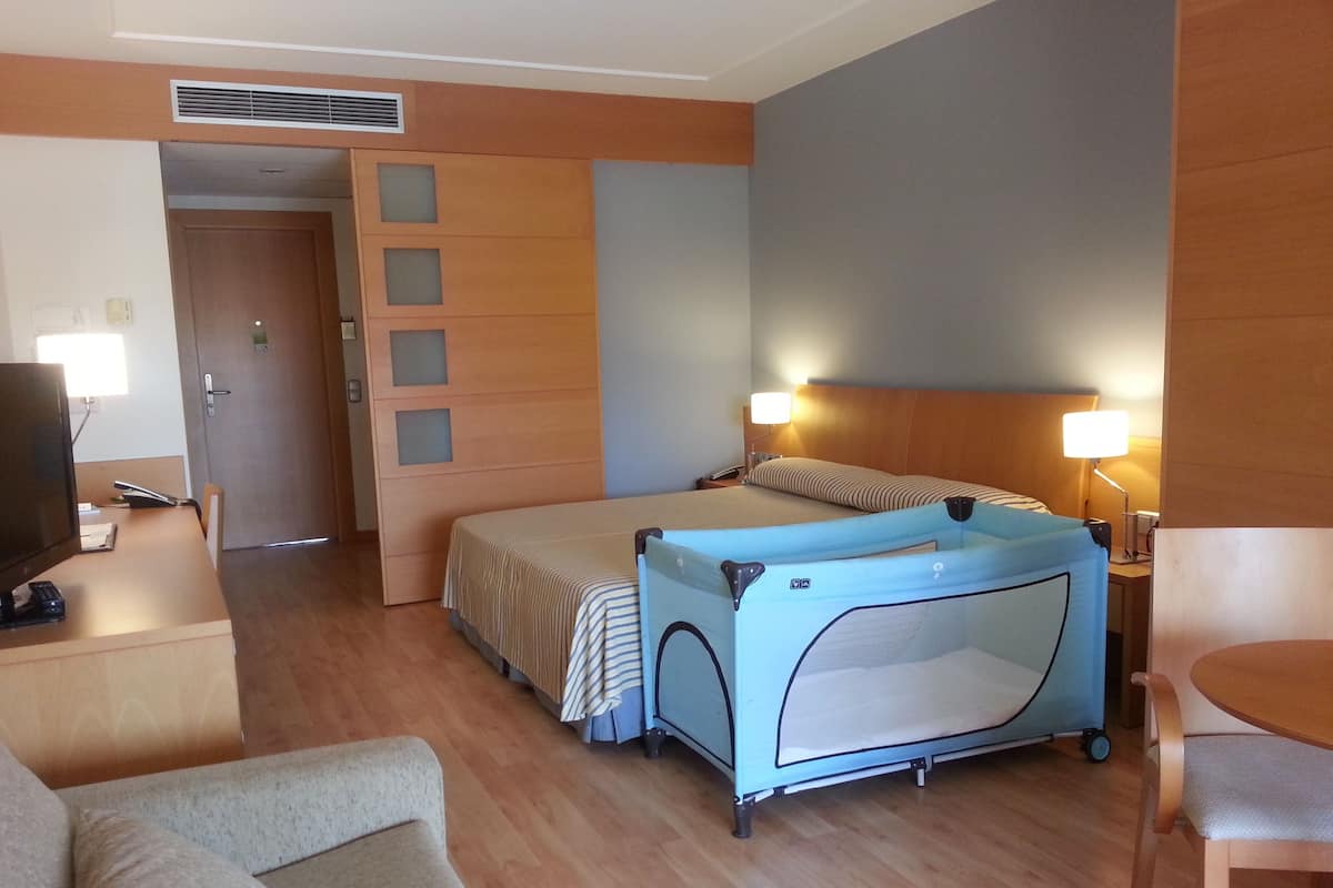 Une chambre d’hôtel comprenant un lit, un bureau avec un ordinateur, une chaise, une petite table et un berceau.