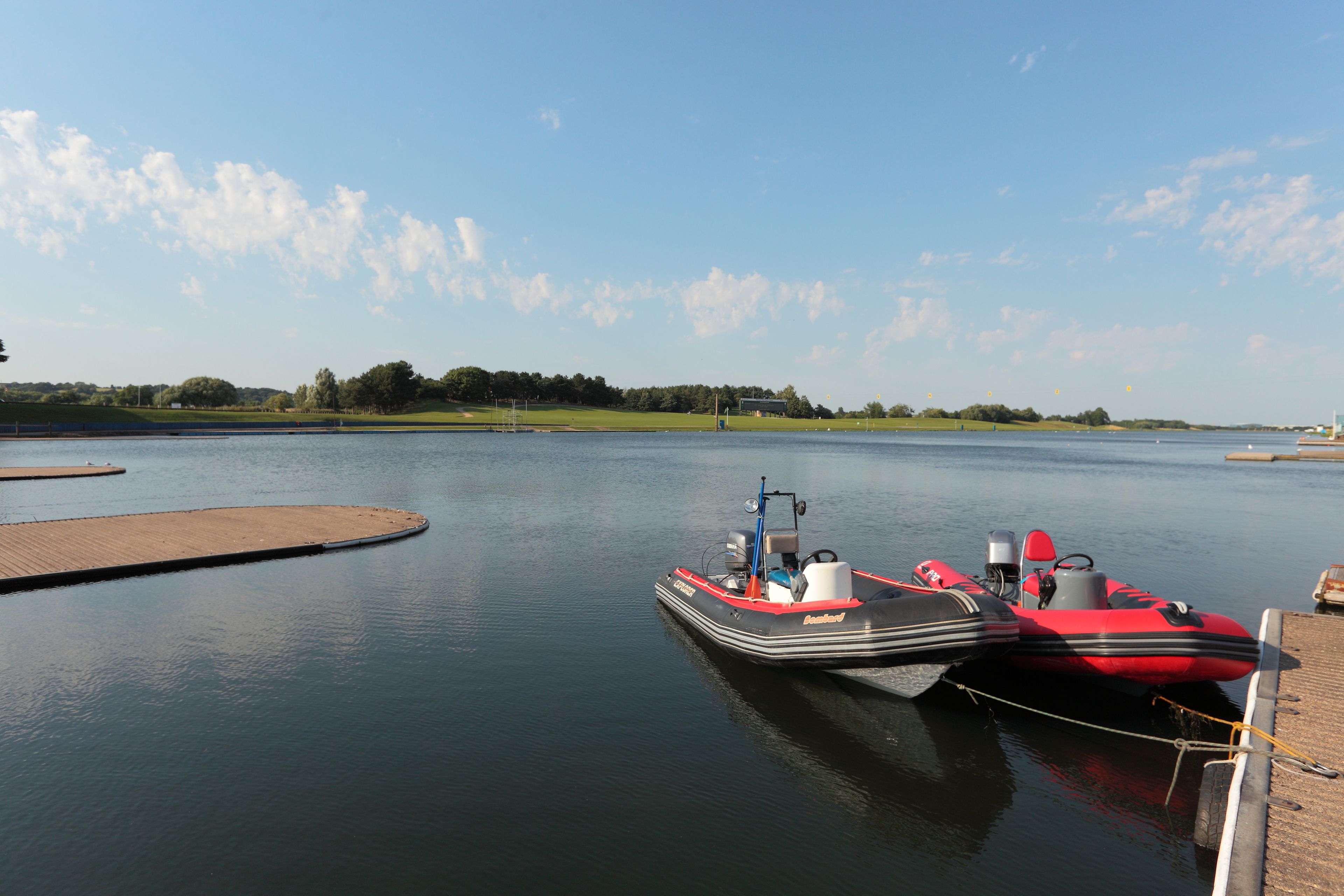 Een rustig meer met een steiger en een rode en zwarte opblaasbare boot eraan vastgemaakt.