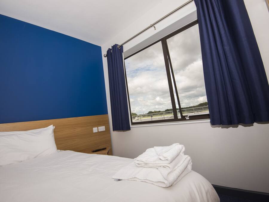 Habitación de hotel con cama, ventana con cortinas y vista a un cielo nublado.