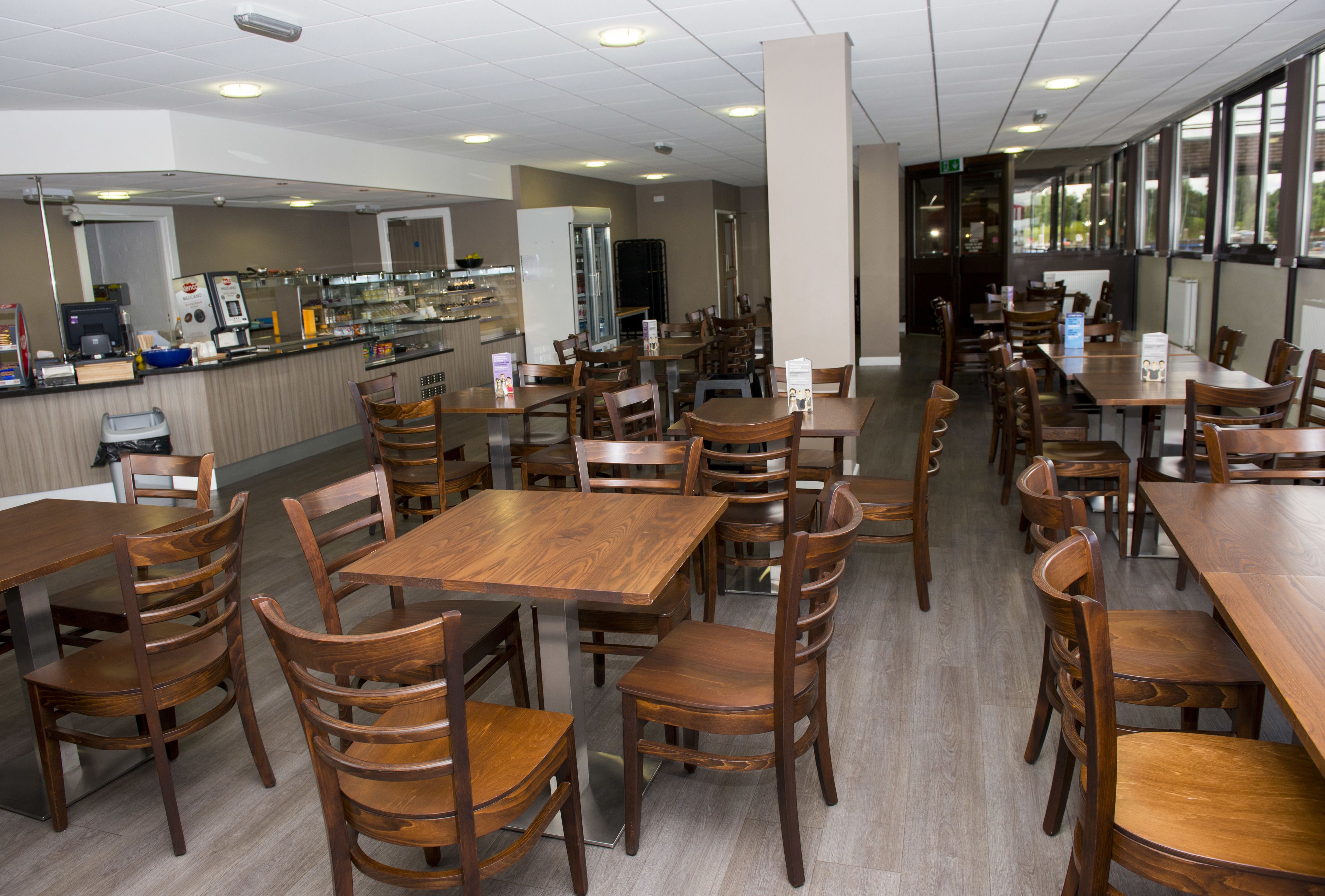 Un ristorante spazioso con tavoli e sedie di legno, un bancone con distributore di bevande e ampie finestre che lasciano entrare luce naturale.