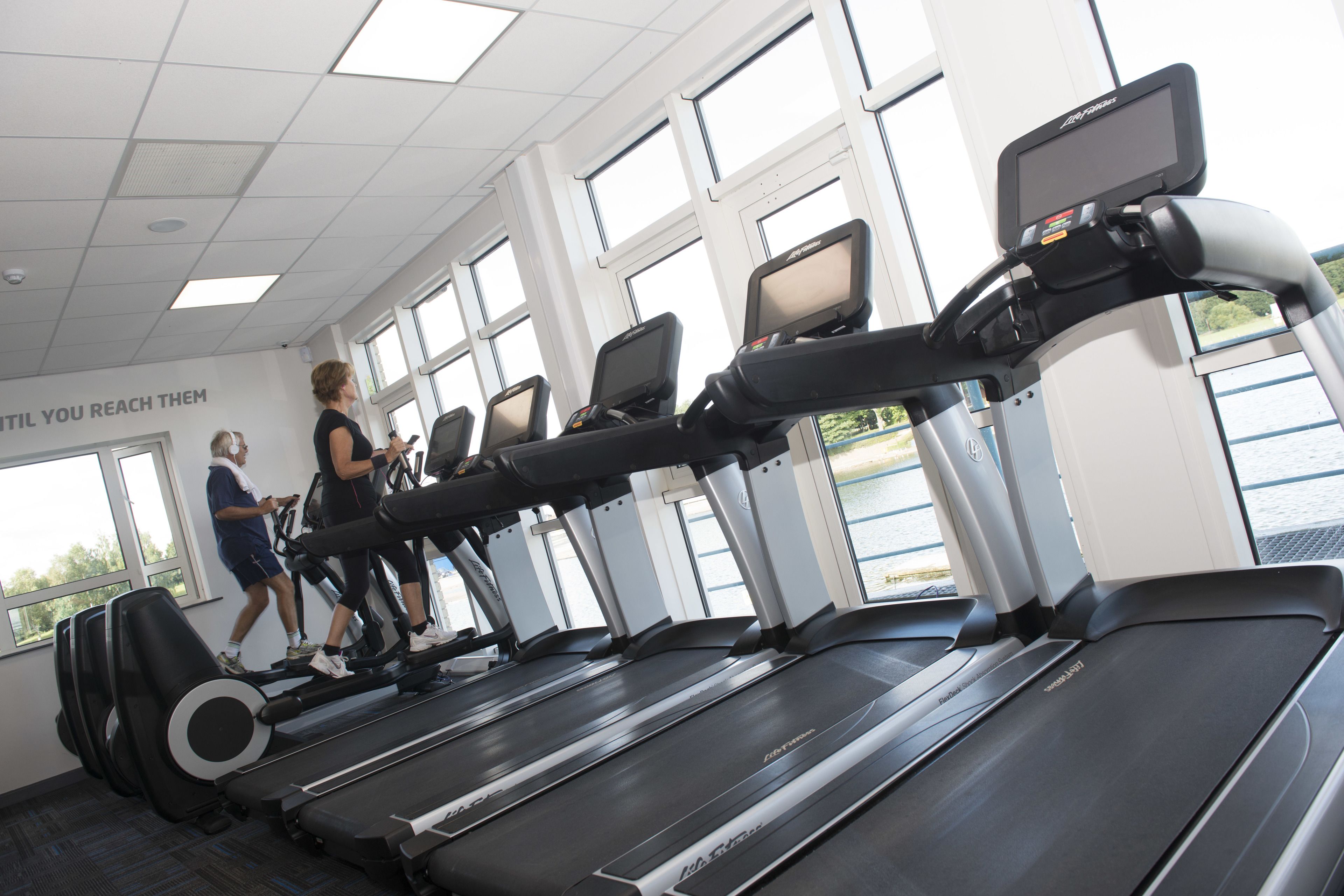 A gym with treadmills, large windows, and a motivational quote on the wall.