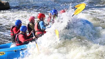 A group of people in a blue raft navigating through rough waters, wearing helmets and life jackets.