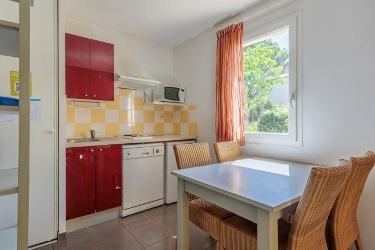 A compact kitchen with red cabinets, a microwave, and a dining area with wicker chairs.