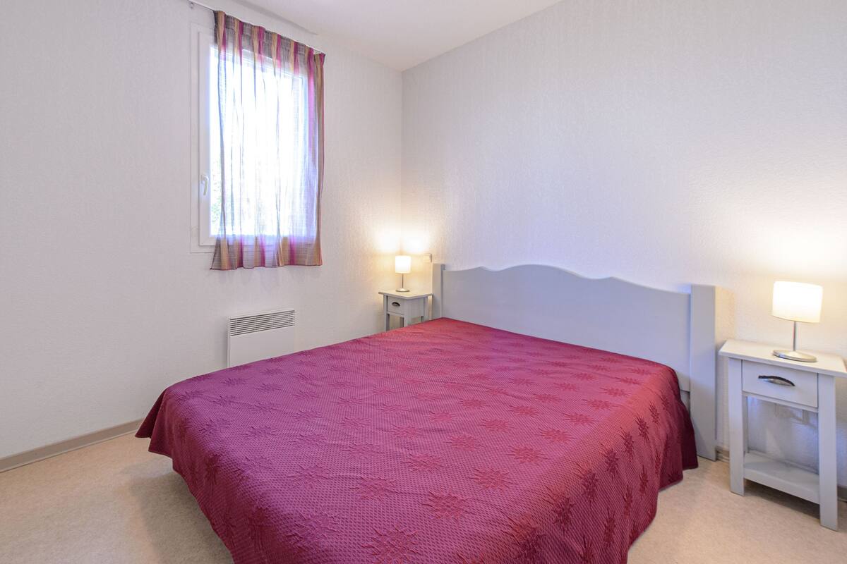 A bedroom with a bed, two bedside tables with lamps, a radiator, and a window with curtains.