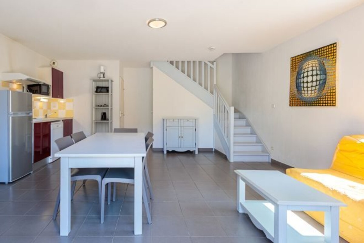A modern kitchen with white cabinetry, a dining table with chairs, a staircase, and a yellow sofa.