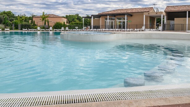 Una piscina con sillones de descanso y un edificio con tejado de azulejos.