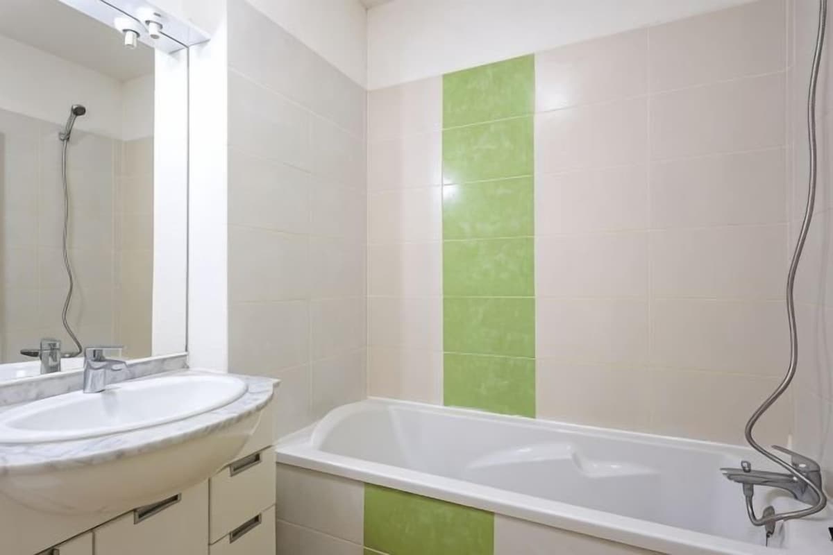 A bathroom with a white sink, a bathtub, and a green vertical tile accent.