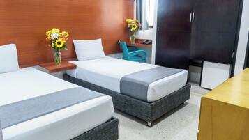 A hotel room with two beds, a wooden headboard, a desk with a chair, a vase with flowers, and a wardrobe.