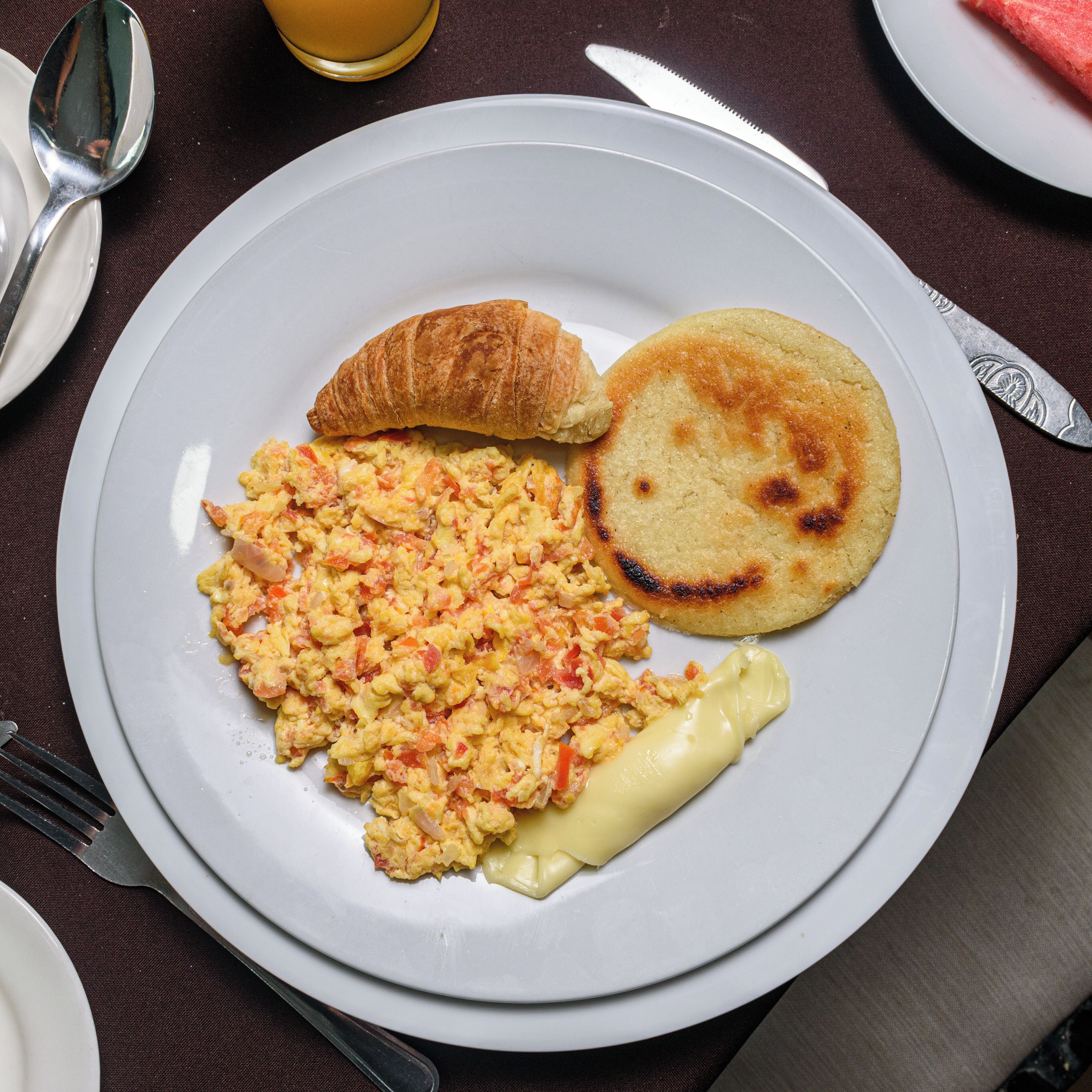 A plate with scrambled eggs, a croissant, and a small pancake on a table.