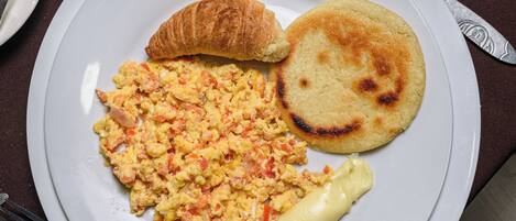 A plate with scrambled eggs, a croissant, and a small pancake on a table.
