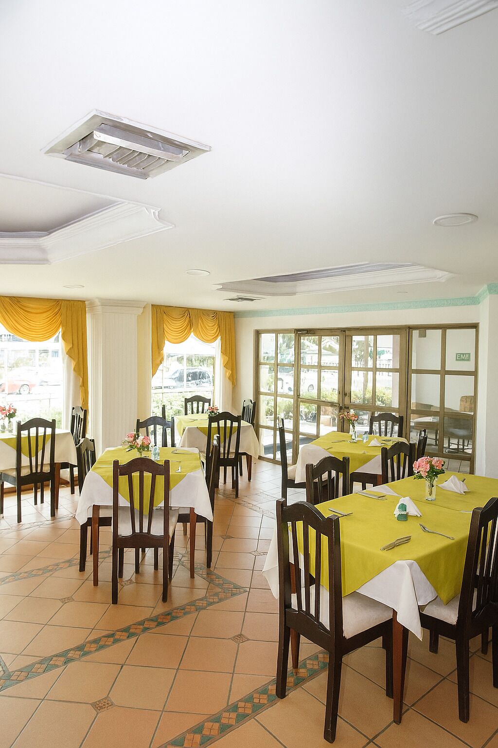 A dining area with tables set for four, chairs, and a view through large windows.