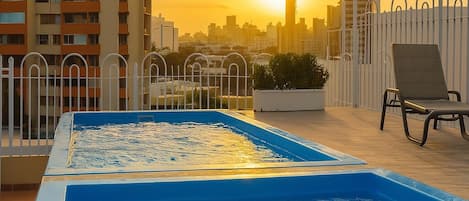 A rooftop pool with a city skyline in the background during sunset.