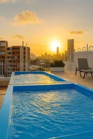 Piscina no terraço com o horizonte da cidade ao fundo durante o pôr do sol.