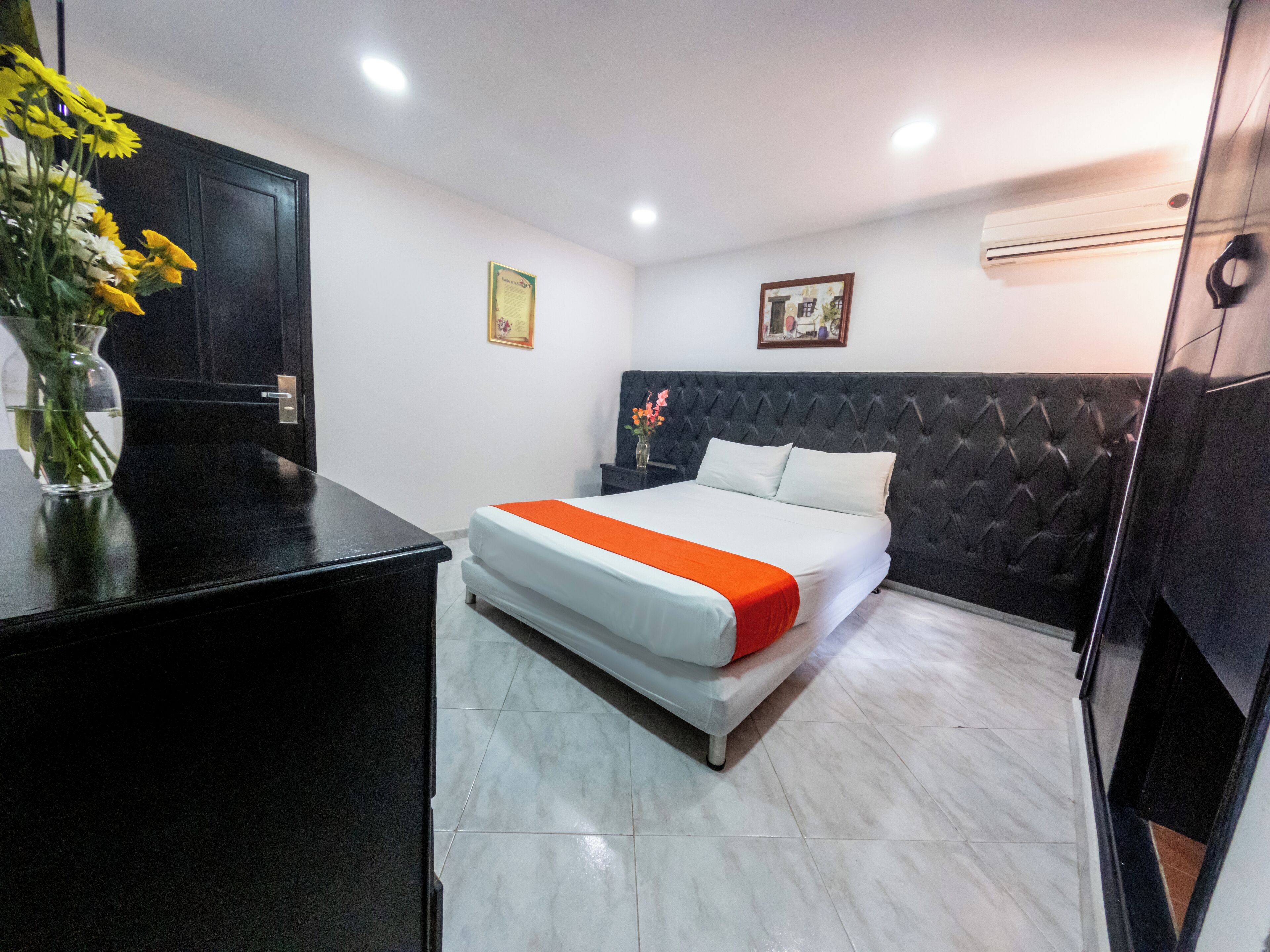 Una habitación de hotel con una cama, una mesita de noche, un jarrón con flores y una puerta.