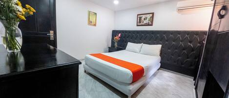 Una habitación de hotel con una cama, una mesita de noche, un jarrón con flores y una puerta.