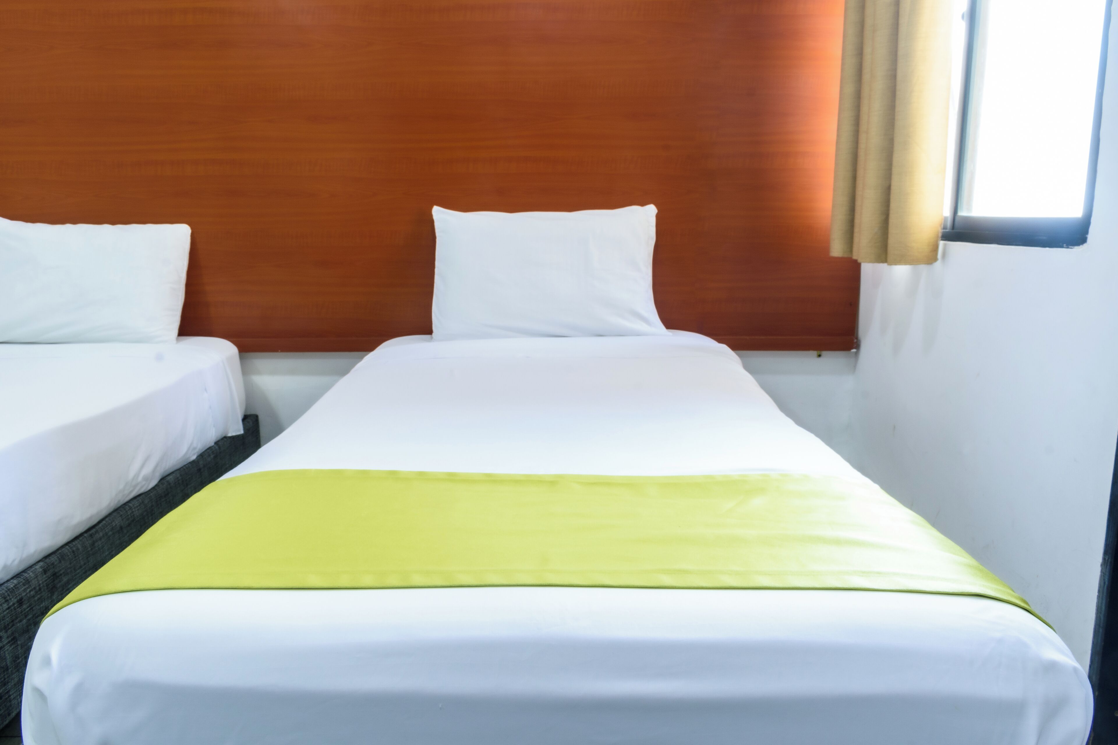 Une chambre d’hôtel avec deux lits simples, une tête de lit en bois et une fenêtre avec des rideaux.