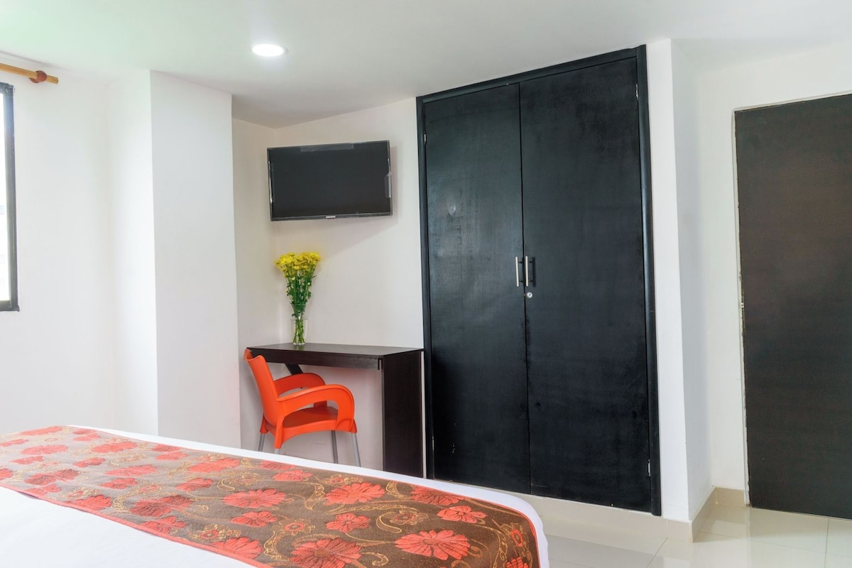 A bedroom with a bed, a desk with a chair, a wardrobe, and a TV on the wall.