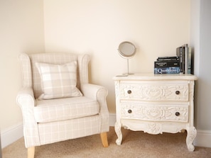 A white armchair with a plaid cushion, a white dresser with ornate carvings, and a small round mirror on top. - Alcuin Lodge (York)