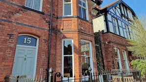 A traditional brick building with a number '15' on the door, a sign above the door, and a window with a curtain. - Alcuin Lodge (York)