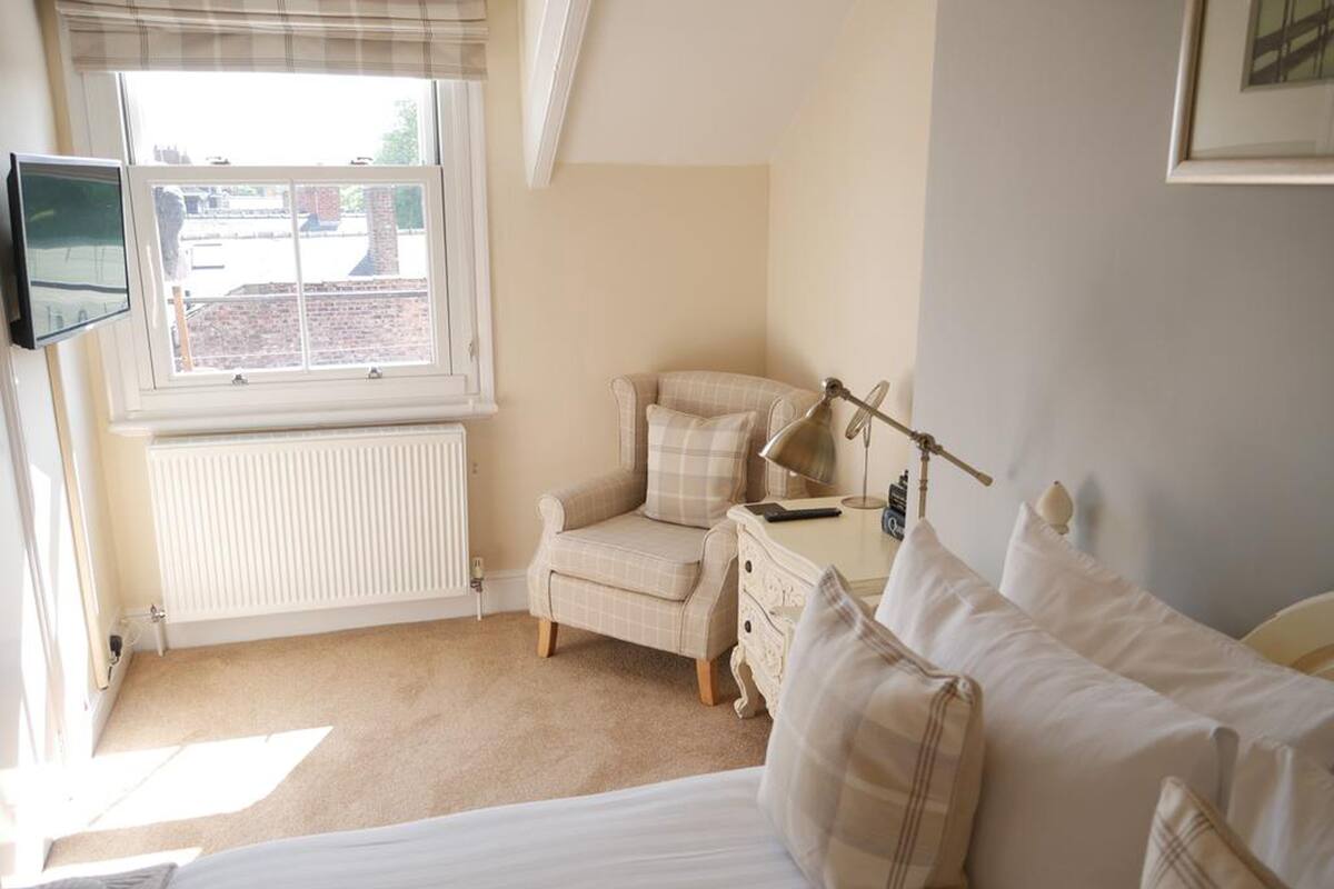 A bedroom with a bed, a chair, a desk, a lamp, and a television on the wall.