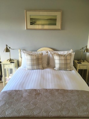A neatly made bed with a patterned bedspread, two bedside tables with lamps, and a framed picture on the wall. - Alcuin Lodge (York)
