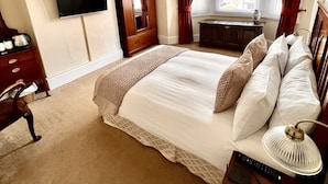 A bedroom with a large bed, a TV mounted on the wall, a wooden wardrobe, and a desk with a chair. - Alcuin Lodge (York)