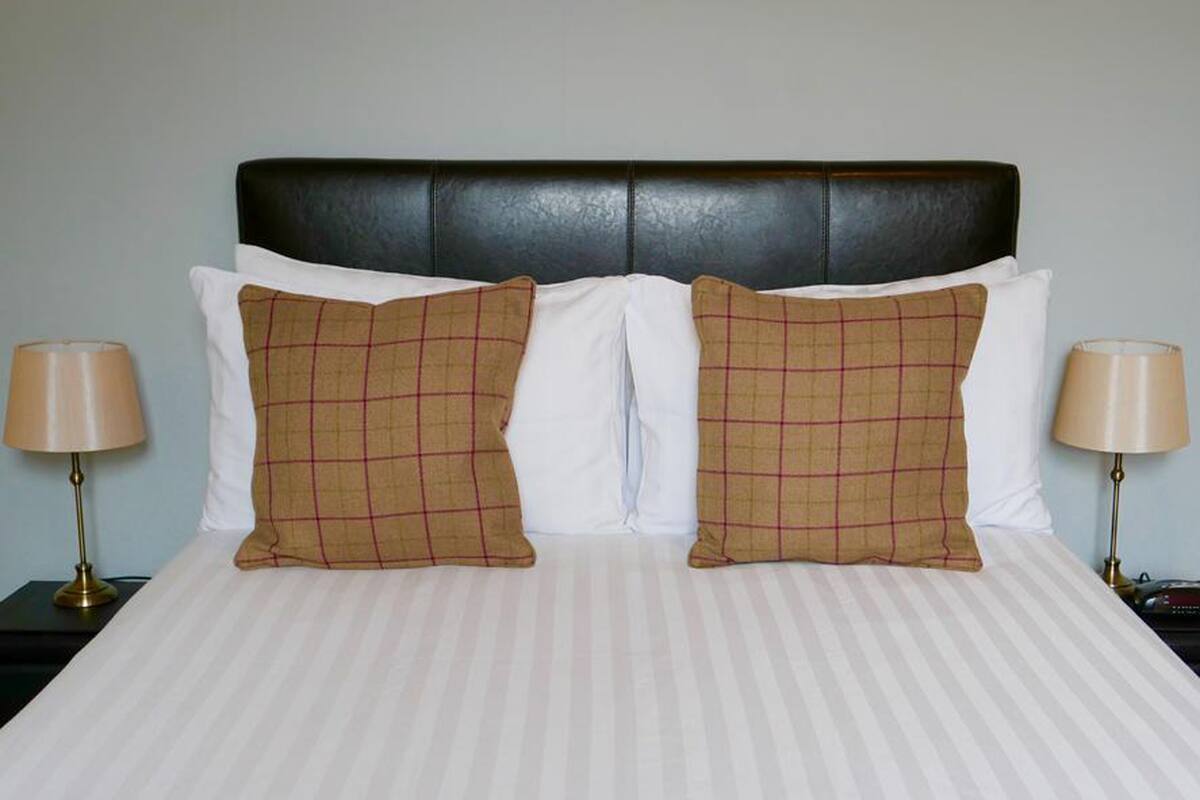 A bed with a striped white bedspread, two brown plaid pillows, and a black upholstered headboard.