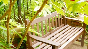 A wooden bench in a lush garden with dense foliage and a metal fence in the background. - Alcuin Lodge (York)