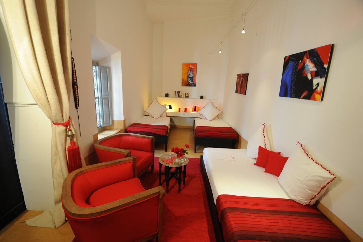 A hotel room with red and white furnishings, a small table with a vase of flowers, and artwork on the walls.