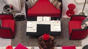 Una habitación con un sofá rojo, una mesa de centro de vidrio y una alfombra estampada.