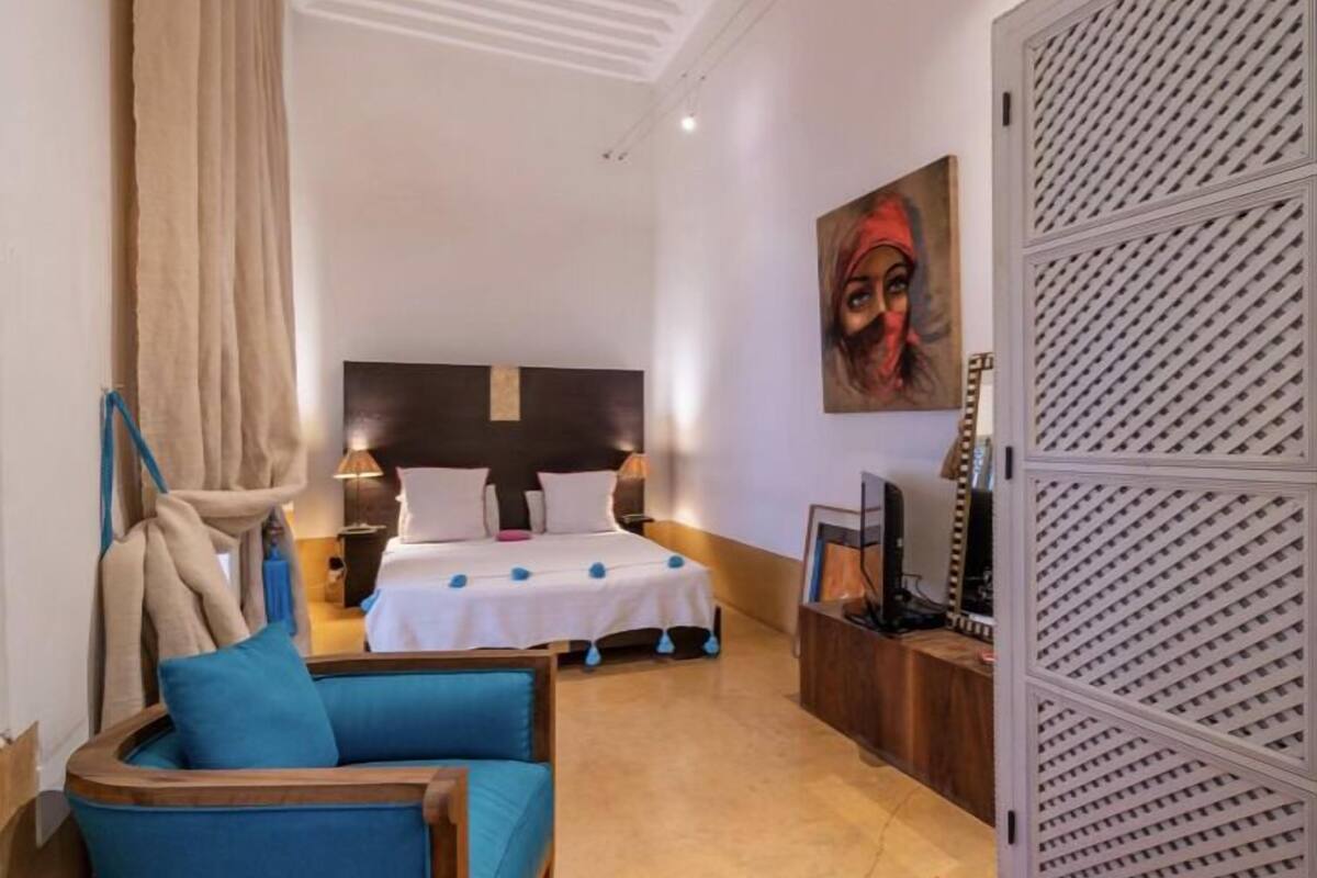 A hotel room with a bed, a desk, a chair, a TV, and a painting on the wall.