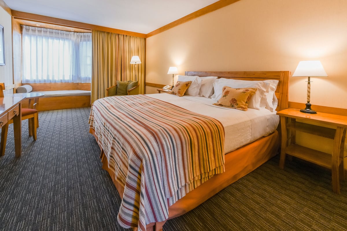 Une chambre d’hôtel avec un grand lit, un bureau, une chaise et une fenêtre avec des rideaux.