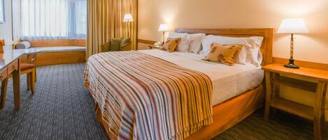 A hotel room with a large bed, a desk, a chair, and a window with curtains.