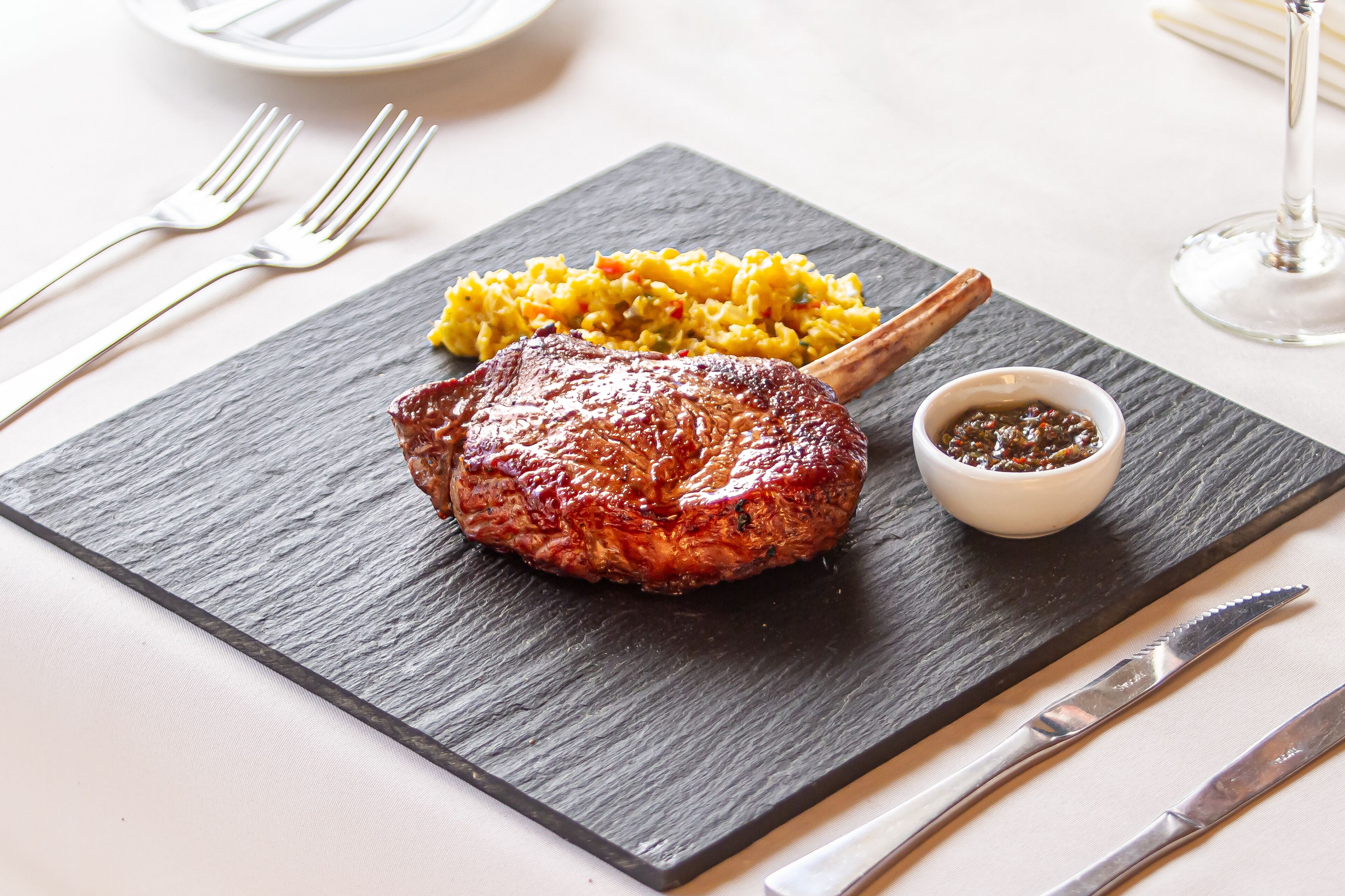 A steak with a side of yellow rice and a small bowl of sauce on a slate serving board.