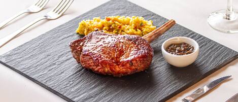 A steak with a side of yellow rice and a small bowl of sauce on a slate serving board.