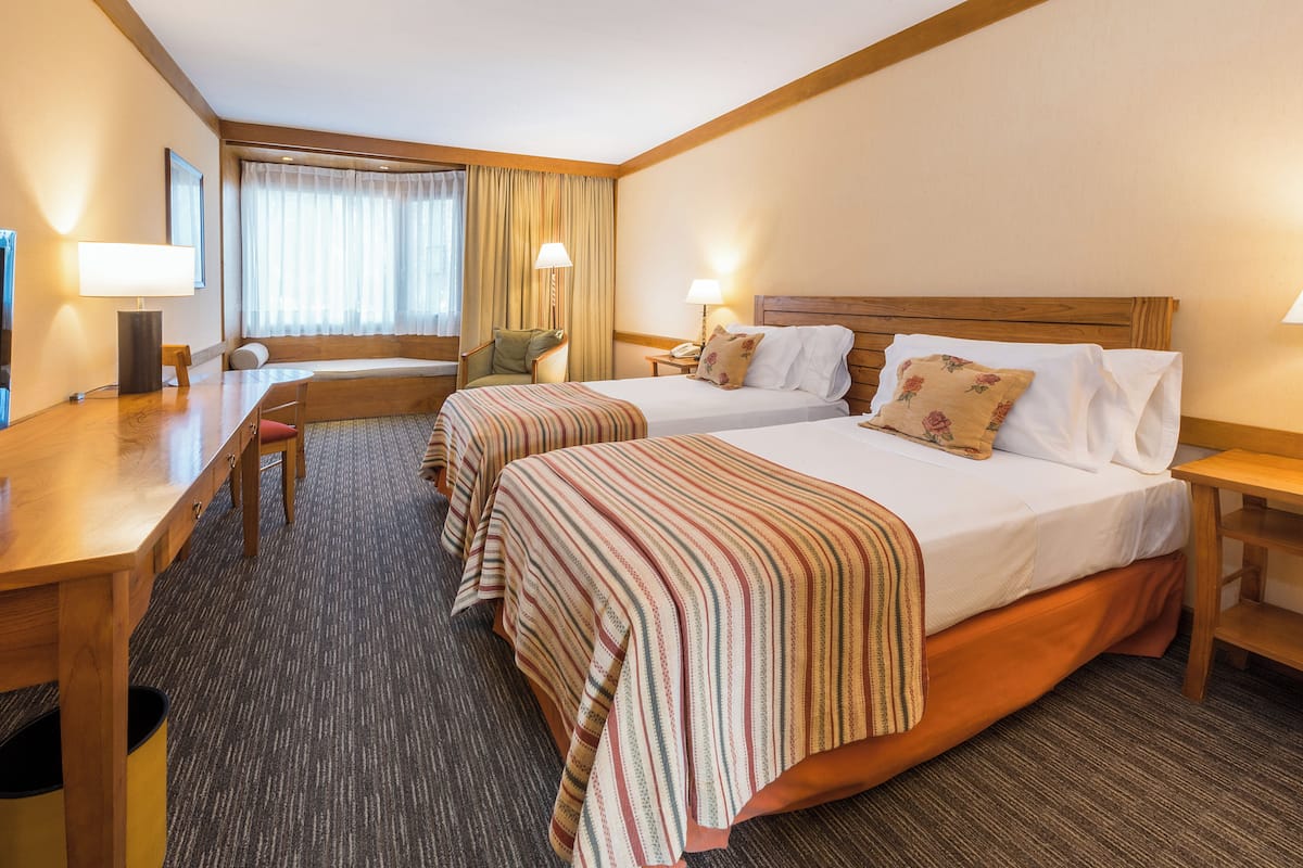 Une chambre d’hôtel avec deux lits, un bureau, une chaise et une fenêtre avec des rideaux.