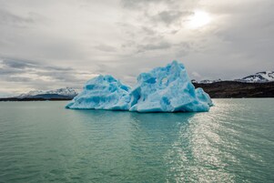 Two large icebergs in a body of water with a mountainous background.