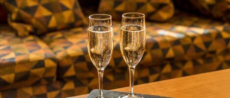 Two glasses of champagne on a slate coaster, with a small plate of chocolates in front.