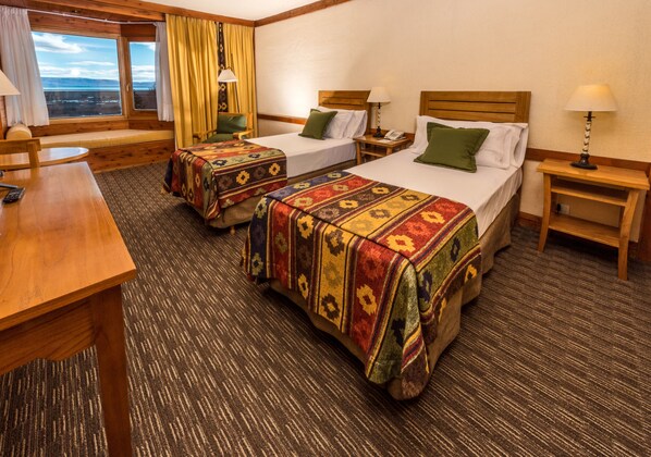 A hotel room with two beds, a wooden desk, and a window with curtains.