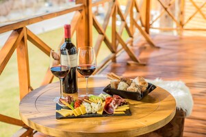 Una mesa de madera con una tabla de embutidos, dos copas de vino y una botella sobre una terraza.