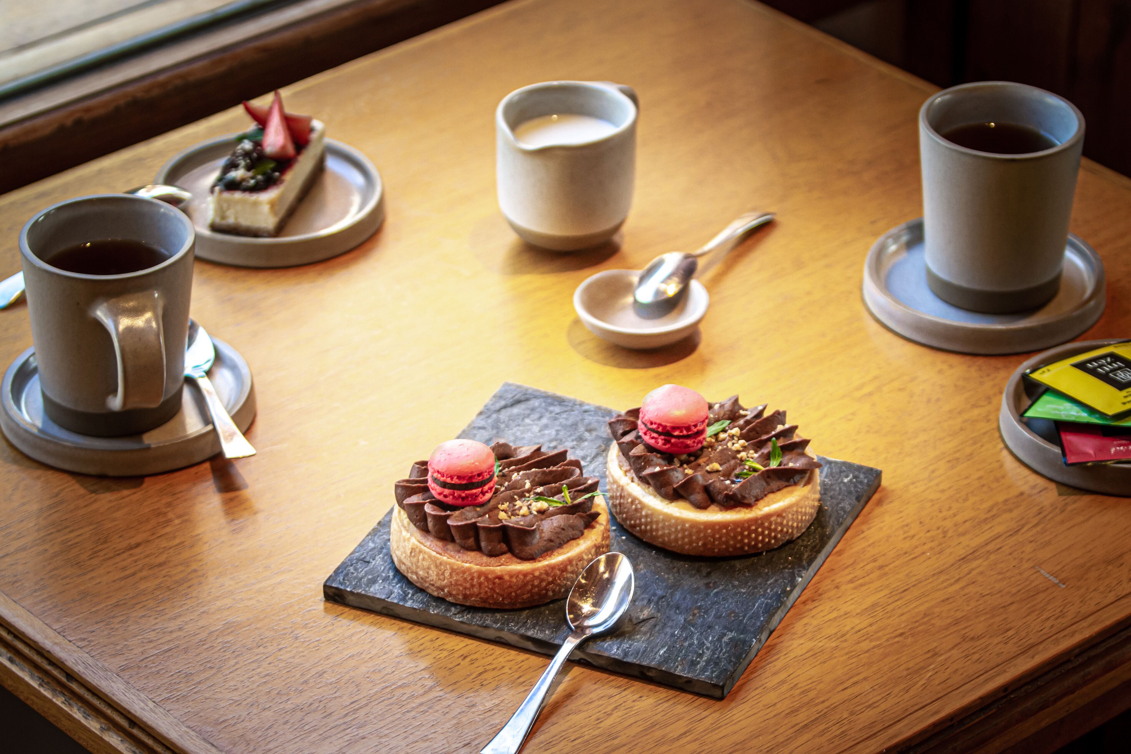 A table with two desserts, two cups of coffee, and a small plate with a spoon.